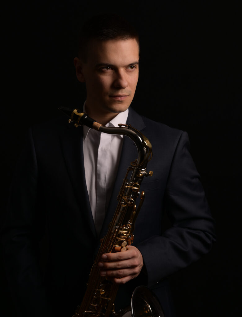 Portret artystyczny mężczyzny w granatowym garniturze trzymającego saksofon podczas sesji fotograficznej w Warszawie